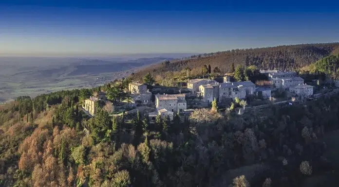 Hotel Monteverdi Experience on the Hilltop of Tuscany Aerial view of Monteverdi Hotel nestled on a Tuscan hillside surrounded by vineyards and cypress trees under a clear blue sky