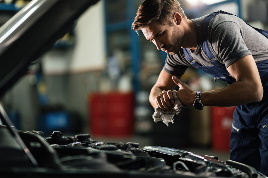 Young auto mechanic cleaning hands after working on car engine in a garage. Young auto mechanic cleaning hands after working on car engine in a garage.