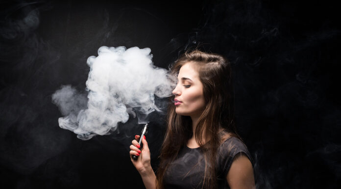 How Has Vaping Evolved Over the Years? Attractive young woman vaping and blowing smoke isolated on black