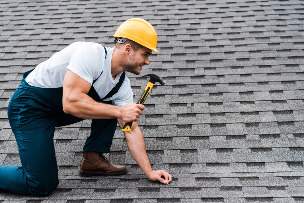 handsome repairman in helmet holding hammer while repairing roof in house. Photo via adobe free stock