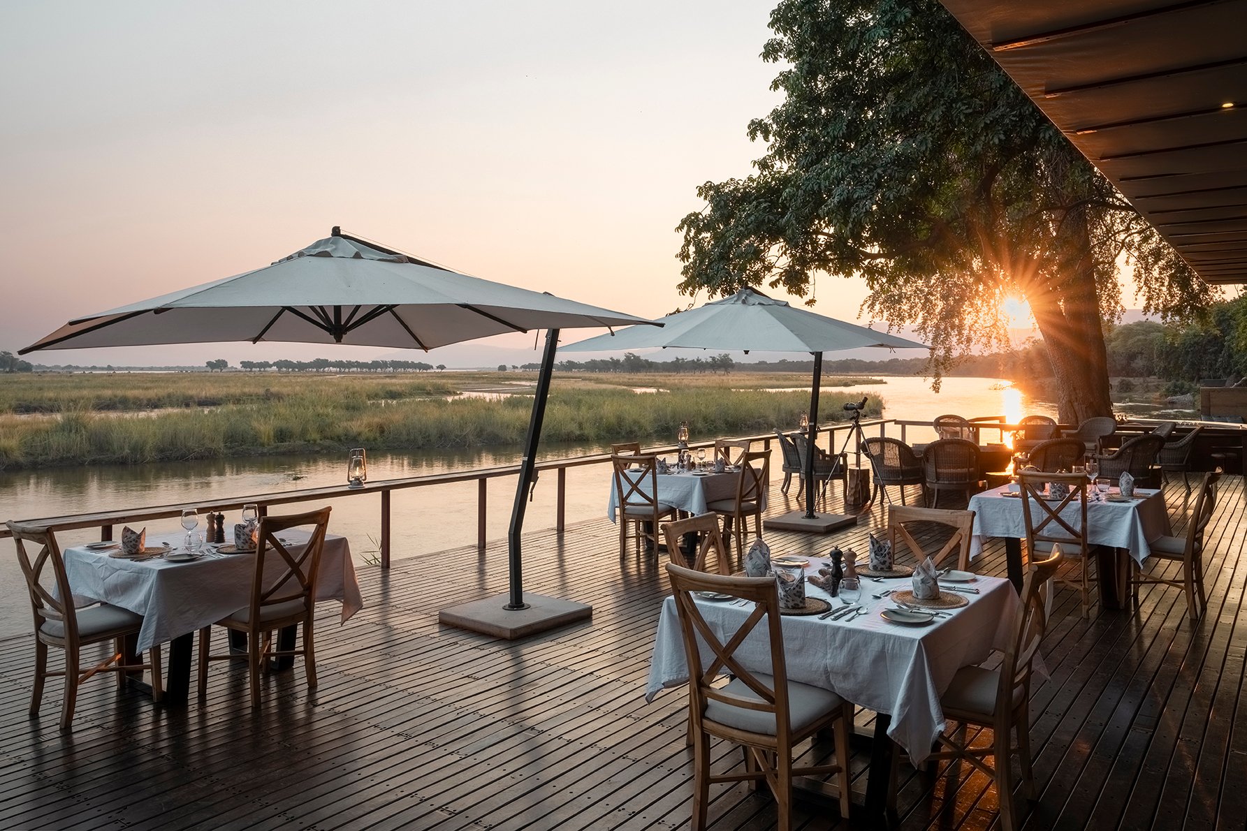 Dining on the main deck with the sun setting. Photo courtesy of Green Safaris | Sausage Tree Camp Dining on the main deck with the sun setting. Photo courtesy of Green Safaris | Sausage Tree Camp