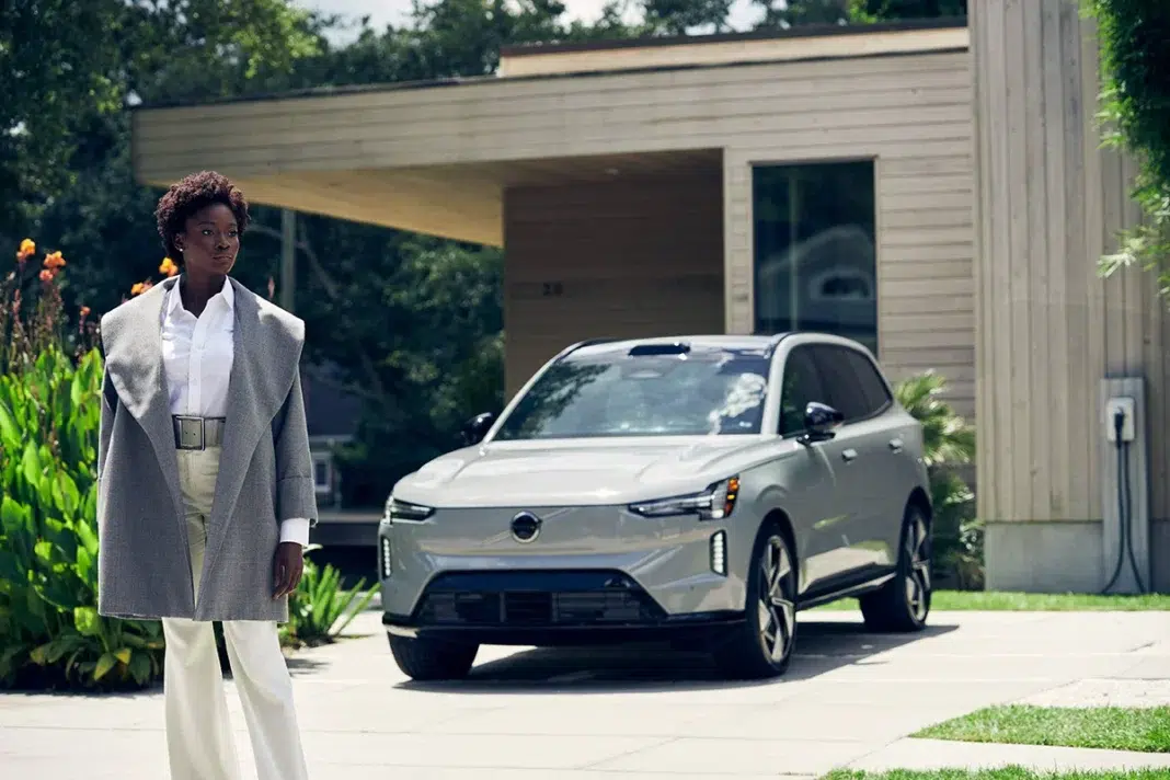 A model wearing the Sergio Hudson tailored wool car coat stands beside the all-electric Volvo EX90, an image of modern Scandinavian design and confidence.