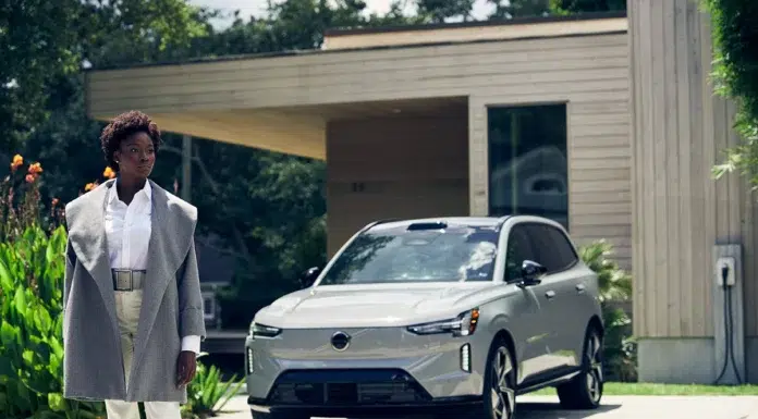 Volvo × Sergio Hudson: Redefining Modern Luxury A model wearing the Sergio Hudson tailored wool car coat stands beside the all-electric Volvo EX90, an image of modern Scandinavian design and confidence.