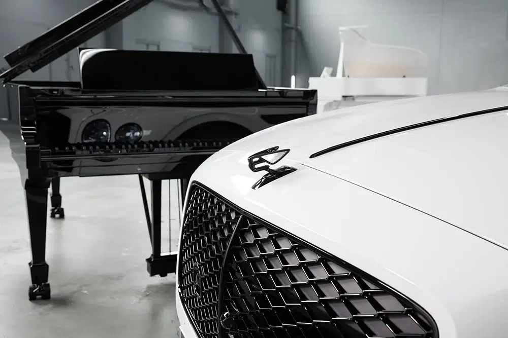 Close-up of Bentley’s signature Flying B emblem and black grille with Steinway’s Ultra Black grand piano in the background, capturing a moment where craftsmanship and performance converge. Close-up of Bentley’s signature Flying B emblem and black grille with Steinway’s Ultra Black grand piano in the background, capturing a moment where craftsmanship and performance converge.