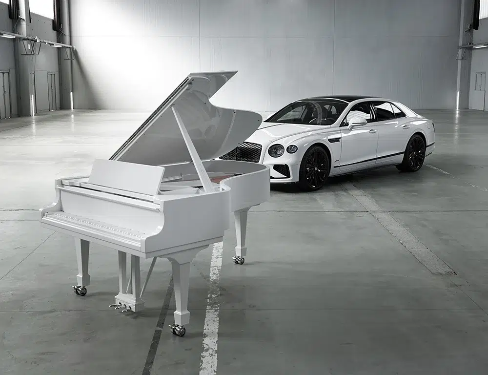 A pristine white Steinway grand piano stands beside the Bentley Flying Spur Speed in Arctic White, an image of harmony between music and motoring mastery. A pristine white Steinway grand piano stands beside the Bentley Flying Spur Speed in Arctic White, an image of harmony between music and motoring mastery.