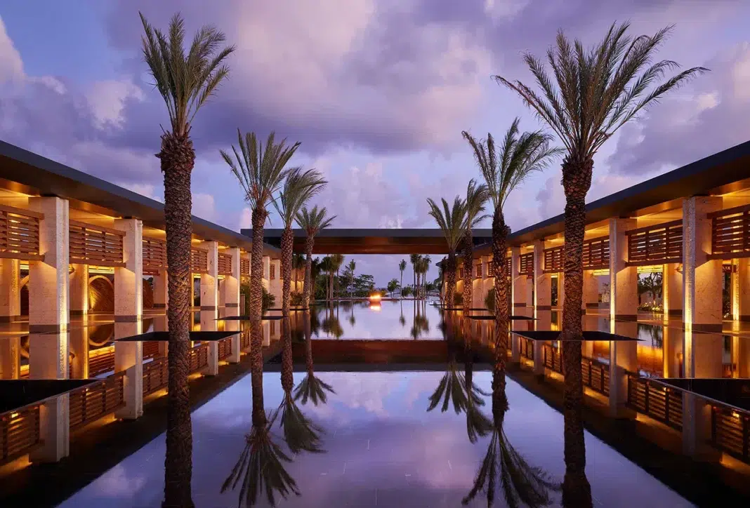 conrad water Elegant resort entrance with palm-lined reflective water feature framed by modern architecture at dusk.