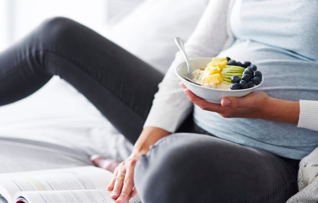 Pregnant woman eating and reading a book at bedroom