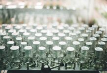 How Premium Supplement Brands Are Really Made Rows of glass supplement bottles on a clean white production line. Photo by Chuttersnap via unsplash